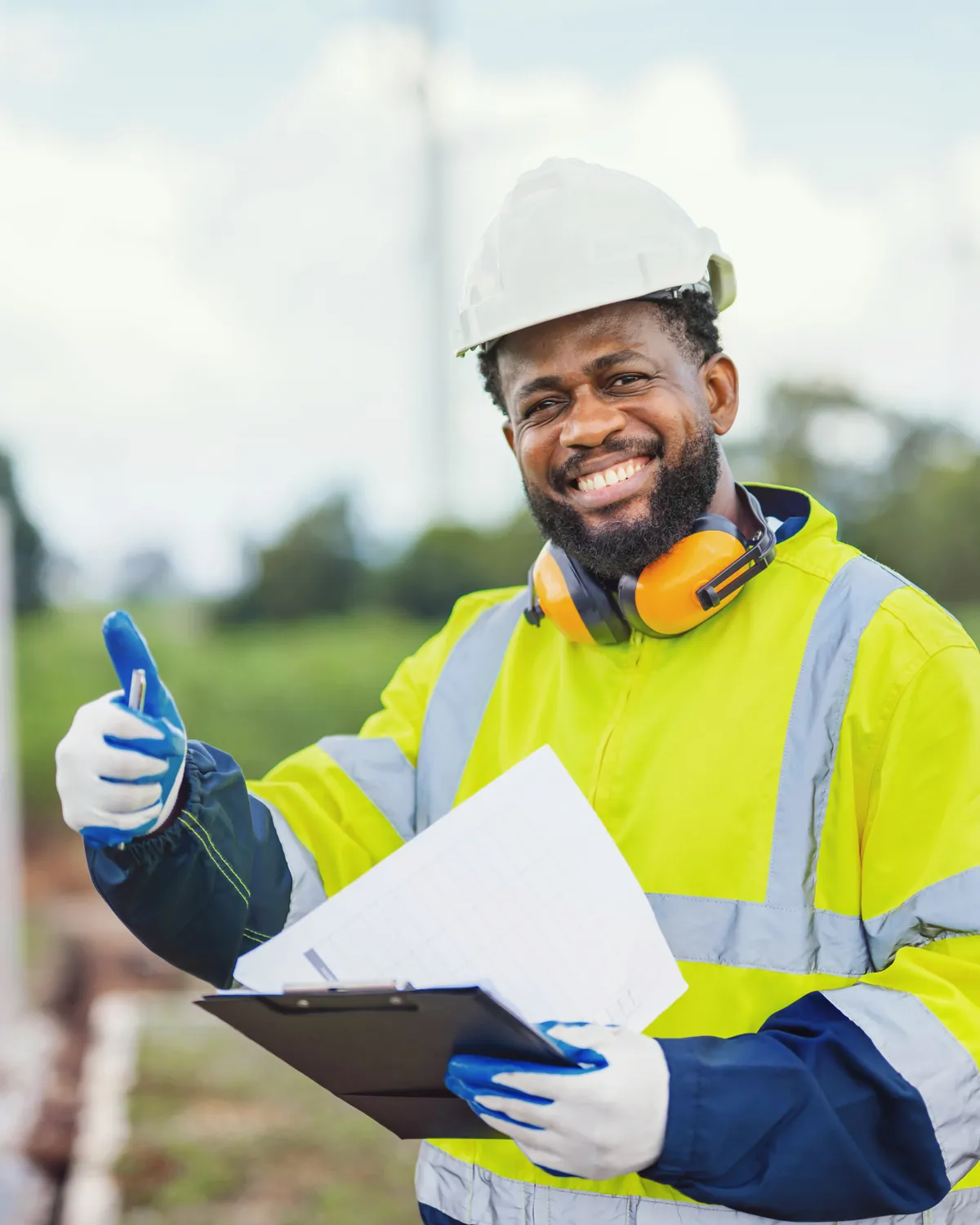 Site safety officer in a hard hat, high-visibility jacket and ear defenders, holding a clipboard